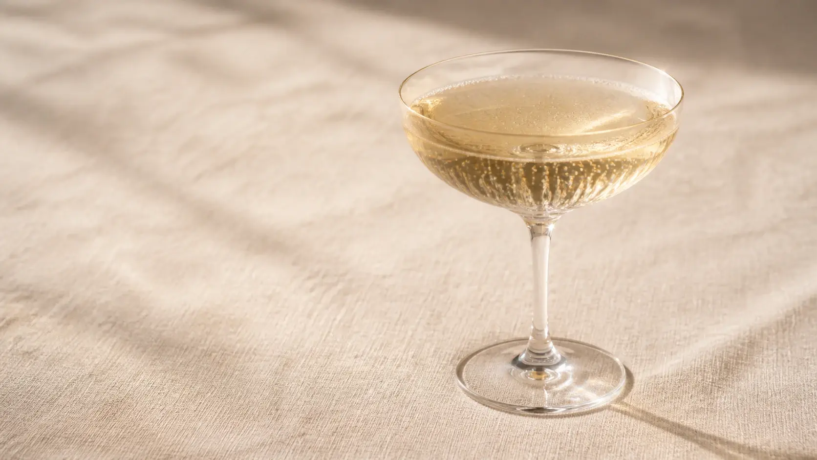 A champagne coupe on linen with the shimmer on its rim and bubbles perfectly balanced